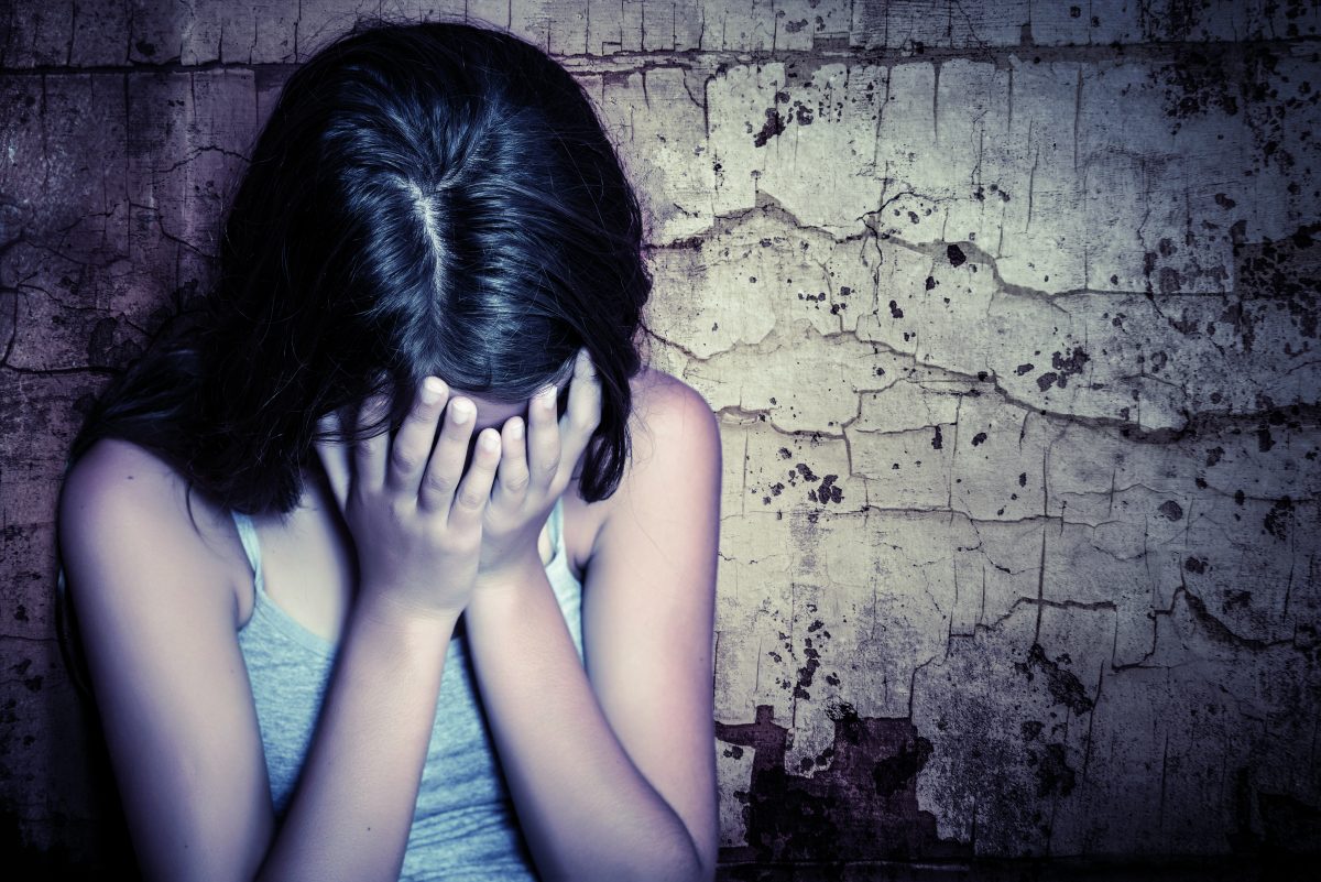 Teenage girl crying sitting on the floor with a grunge wall background